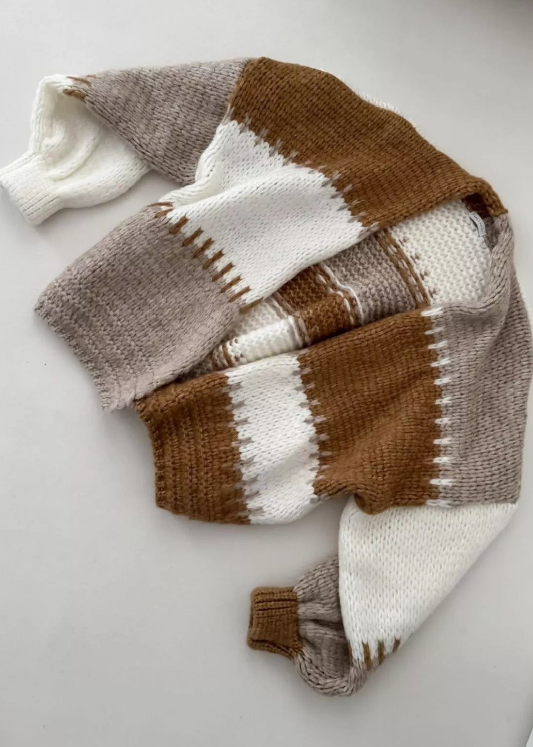 A chunky color block knit cardigan laid flat on a pale surface, sleeves folded across the body