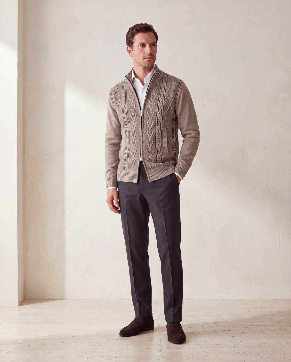 A man in the beige cable pattern zip cardigan, zipped over a white shirt with charcoal trousers and brown suede loafers
